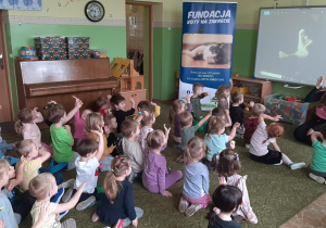 Dzieci siedzą na dywanie i słuchają pogadanki przeprowadzonej przez pracowników fundacji