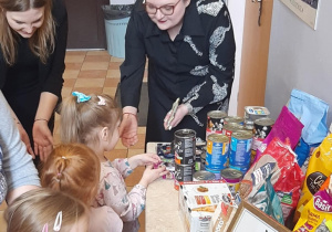 Dzieci i pracownicy fundacji stojący obok stolika, na którym znajduje się karma