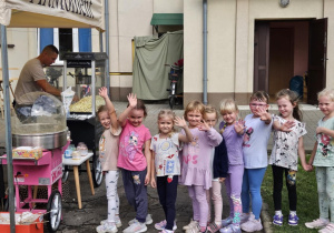 Dzieci stojące w kolejce po watę cukrową machają do kamery