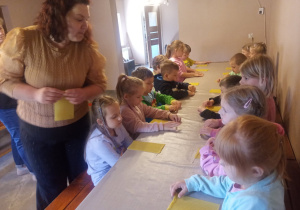 Dzieci przy stolikach wykonują pracę plastyczną.