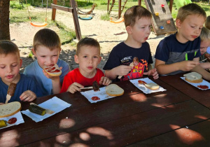 Dzieci przy stoliku jedzą kiełbasę.