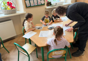 Dzieci przy stolikach wykonują pracę plastyczną.