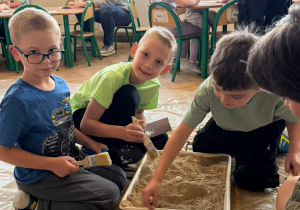 Dzieci na dywanie kopą w pojemniku z piaskiem w poszukiwaniu skarbów