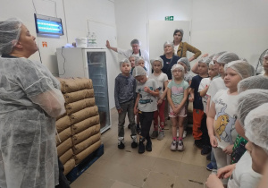 Dzieci znajdują się w hali produkcyjnej i słuchają pracownika manufaktury