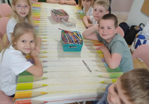 Dzieci siedzą przy stolikach i uśmiechają się do zdjęcia