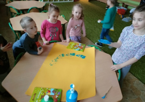 Dziewczynka z grupy 2 odbija dłoń pomalowaną farbą na kartonie.