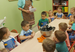 Dzieci z grupy 4 oraz pani, w fartuszkach kuchennych, podczas przygotowywań do wypieku babeczek