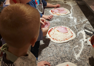 Dzieci układają na pizzy wybrane przez siebie składniki.