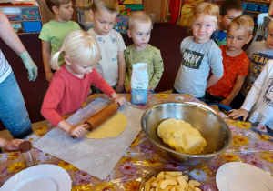 Dziewczynka z grupy 8 wałkuje ciasto drewnianym wałkiem