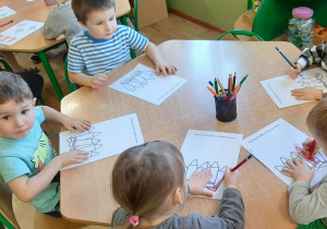 Dzieci z grupy 5 siedzą przy stoliku, kolorują ilustrację kredek