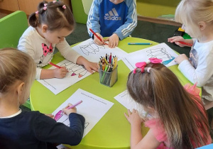 Dzieci z grupy 9 siedzą przy stoliku, kolorują ilustrację kredek