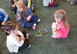 Dzieci układają na dywanie kształt domku z kredek