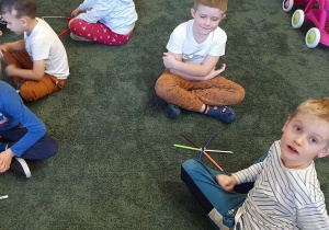 Dzieci układają na dywanie kształt kwiatka z kredek
