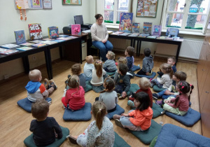 Dzieci siedzą na poduchach, słuchają bajki czytanej przez panią bibliotekarkę