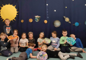 Dzieci z grupy 4 prezentują swoje prace plastyczne - Kolorowe planety - na tle kosmicznej dekoracji, Ukłądu Słonecznego na granatowym tle