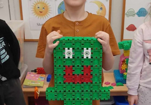 Chłopiec prezentuje uśmiechniętego ufoludka zbudowanego z klocków