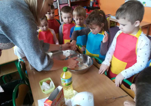 Dzieci z grupy pod okiem nauczyciela dodaja kolejne składniki potrzebne do wykonania babeczek.