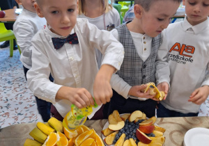 Dzieci jedzą przygotowane na talerzach różne owoce.