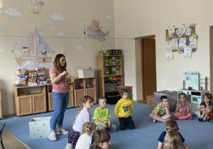 Dzieci siedzące w kole na dywanie słuchające gościa