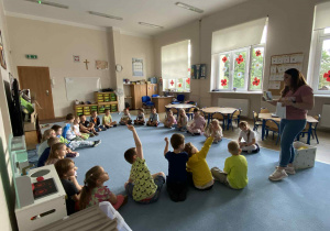 Dzieci siedzące w kole na dywanie słuchające gościa