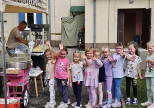 Dzieci stojące w kolejce po watę cukrową machają do kamery