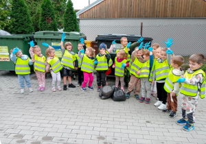 Grupa przedszkolna ustawiona na tle śmietnika trzymająca w rękach worki na śmieci