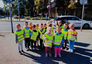 Grupa przedszkolna ustawiona na tle śmietnika trzymająca w rękach worki na śmieci