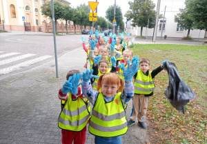Grupa przedszkolna ustawiona na tle śmietnika trzymająca w rękach worki na śmieci