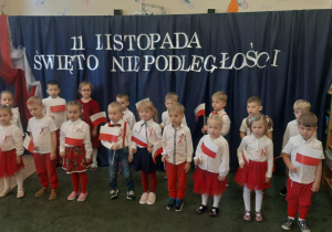 Grupa dzieci ubranych w stroje barwy biało-czerwone na tle dekoracji o charakterze patriotycznym