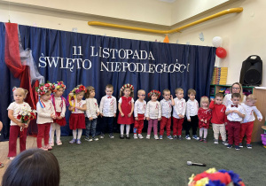 Grupa dzieci ubranych w stroje barwy biało-czerwone na tle dekoracji o charakterze patriotycznym