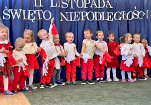 Grupa dzieci ubranych w stroje barwy biało-czerwone na tle dekoracji o charakterze patriotycznym