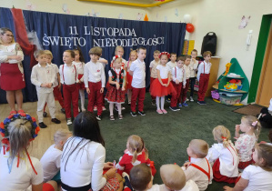 Grupa dzieci ubranych w stroje barwy biało-czerwone na tle dekoracji o charakterze patriotycznym