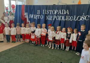 Grupa dzieci ubranych w stroje barwy biało-czerwone na tle dekoracji o charakterze patriotycznym