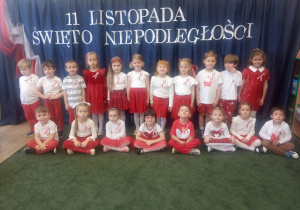 Grupa dzieci ubranych w stroje barwy biało-czerwone na tle dekoracji o charakterze patriotycznym