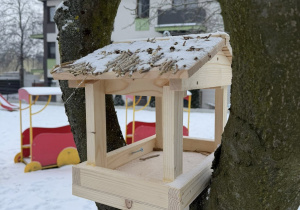 Zdjęcie przedstawia eko - karminik dla ptaków zawieszone na drzewie w przedszkolnym ogrodzie.