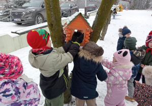 Zdjęcie przedstawia dzieci wsypujące ziarna do karmnika dla ptaków.