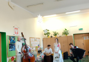 Grupa muzyków wraz z tancerką występująca w sali przedszkolnej przed dziećmi