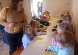Dzieci przy stolikach wykonują pracę plastyczną.
