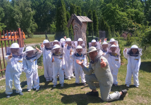 Grupowe zdjęcie dzieci w kombinezonach pszczelarskich.
