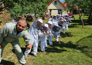 Grupowe zdjęcie dzieci w kombinezonach pszczelarskich.