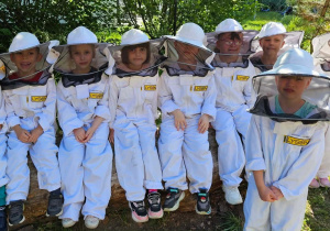 Grupowe zdjęcie dzieci w kombinezonach pszczelarskich.