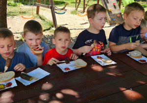 Dzieci przy stoliku jedzą kiełbasę.