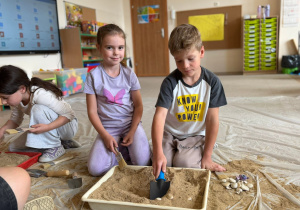Dzieci na dywanie kopą w pojemniku z piaskiem w poszukiwaniu skarbów