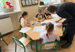 Dzieci przy stolikach wykonują pracę plastyczną.