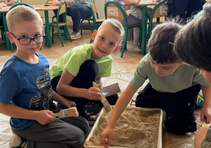 Dzieci na dywanie kopą w pojemniku z piaskiem w poszukiwaniu skarbów