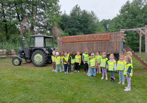 Grupowe zdjęcie dzieci ubranych w kamizelki odblaskowe na tle napisu "Michałówka"