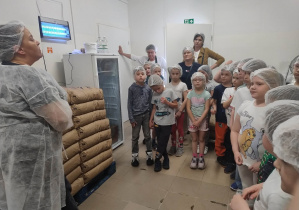 Dzieci znajdują się w hali produkcyjnej i słuchają pracownika manufaktury