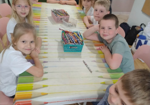 Dzieci siedzą przy stolikach i uśmiechają się do zdjęcia