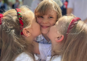 Dwie dziewczynki ubrane w stroje biało-czerwone całują chłopca