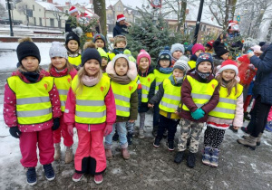 Zdjęcie przedstawia dzieci z grupy 4 z ozdobioną choinką znajdującą się w parku miejskim